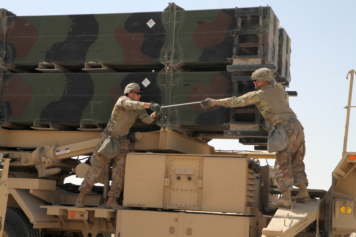 Two soldiers pass a socket wrench during a Patriot missile reload