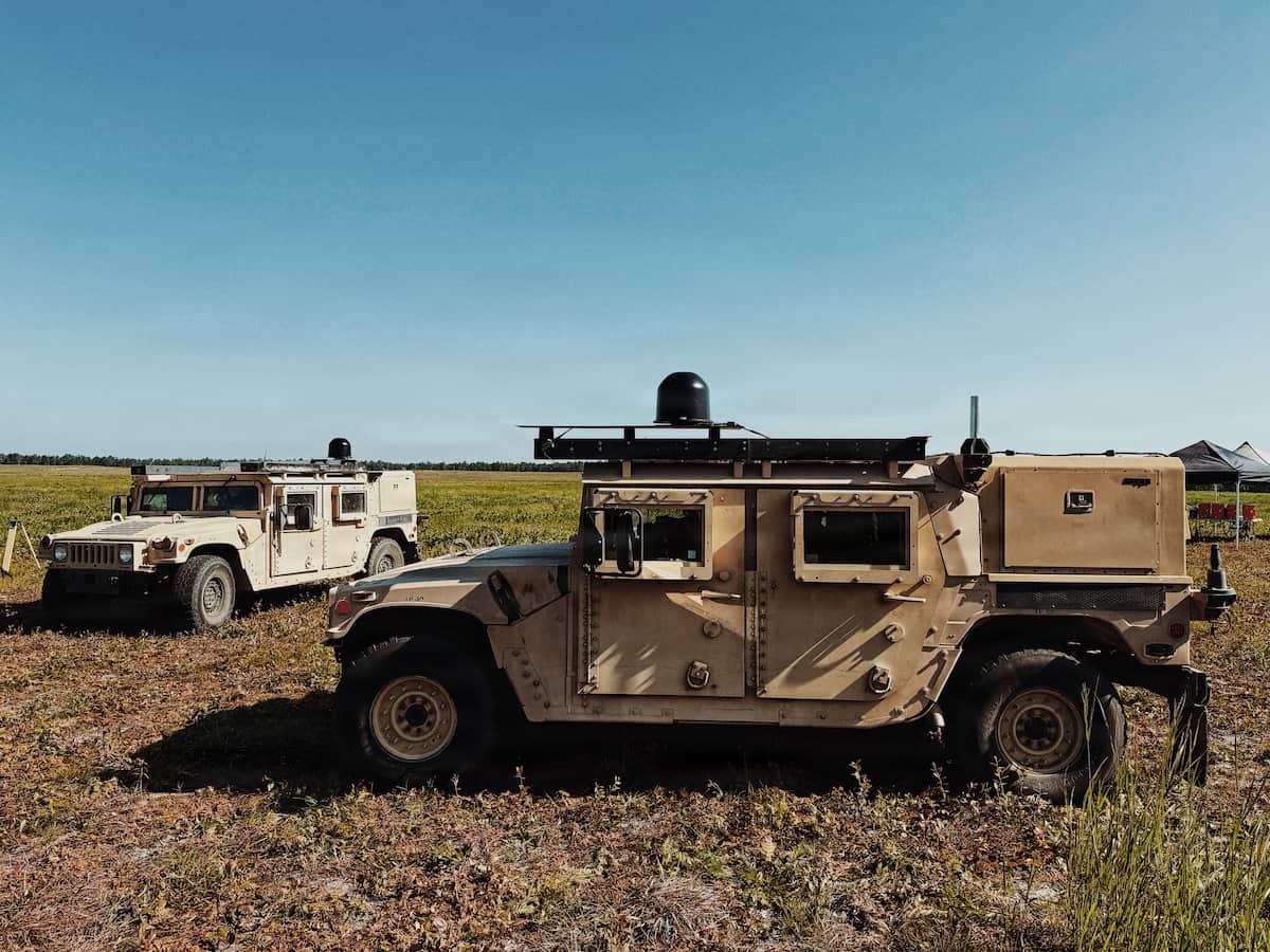 Two Army Humvees parked in a field with Spectrum Situational Awareness System equipment mounted on their roofs
