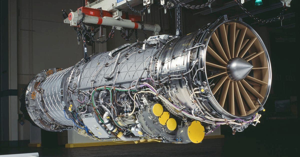 A large adaptive cycle jet engine suspended by chains in a test facility, instrumented with sensors and wiring